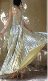 Front swirling view of a metallic champagne gold one-shoulder A-line prom gown with micro-pleated skirt detail